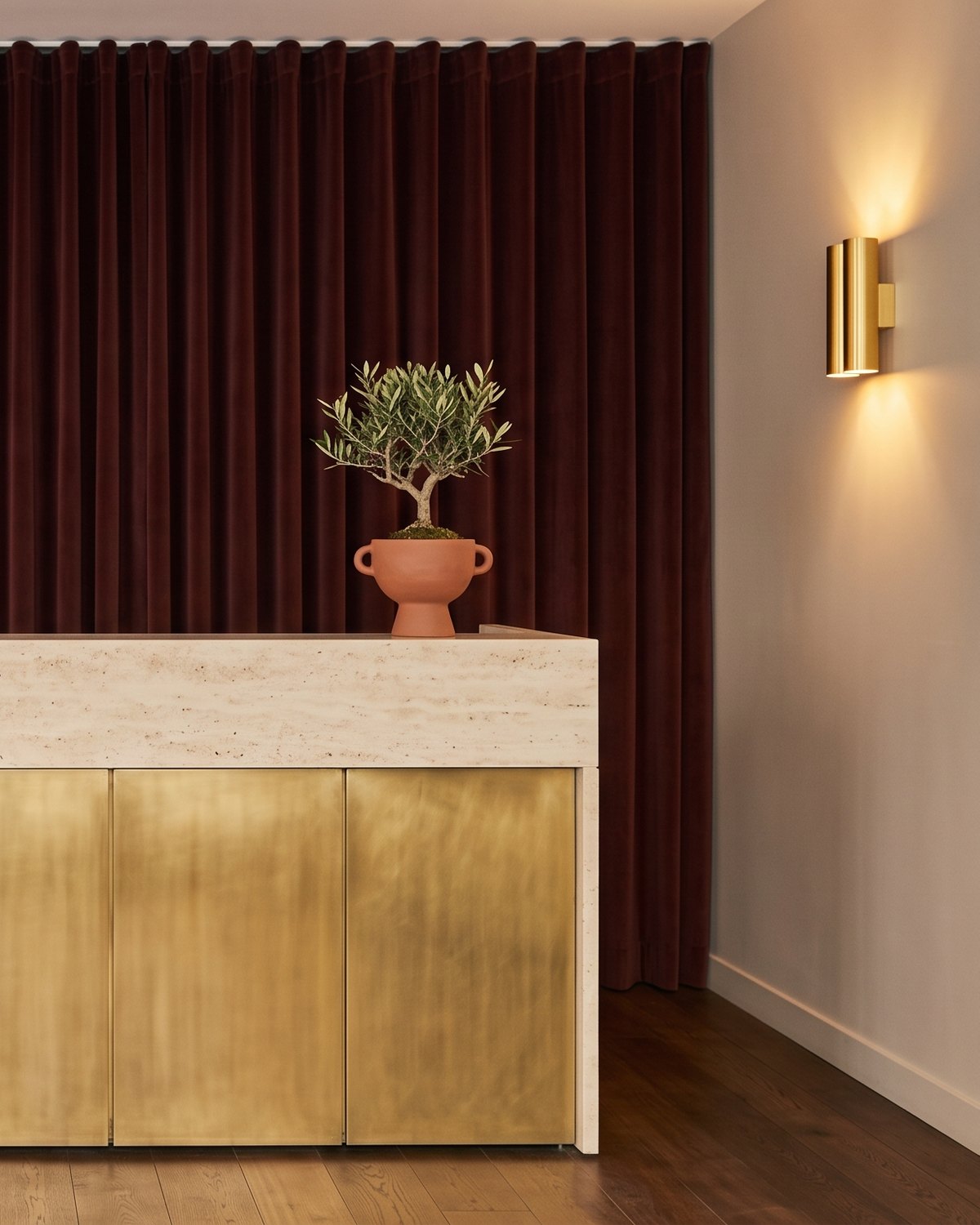 A travertine and brass reception desk beneath a burgundy velvet curtain