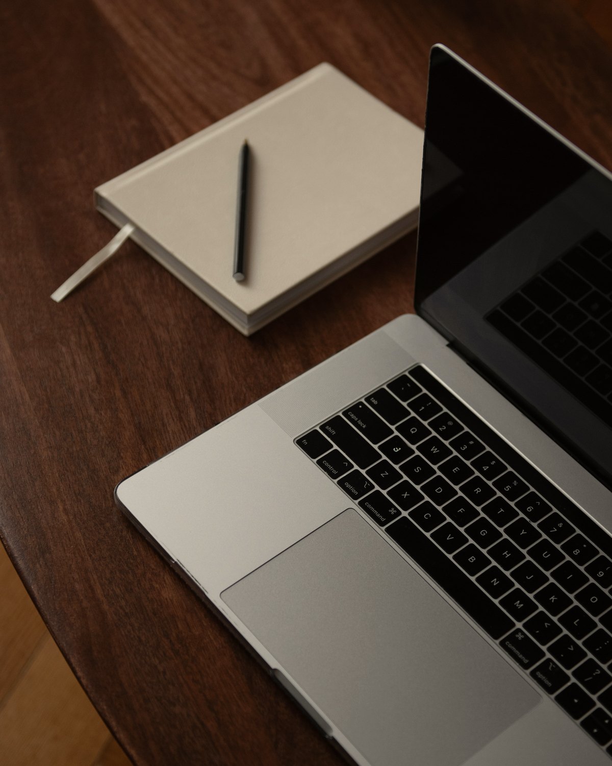 A laptop and notebook on a dark wood desk